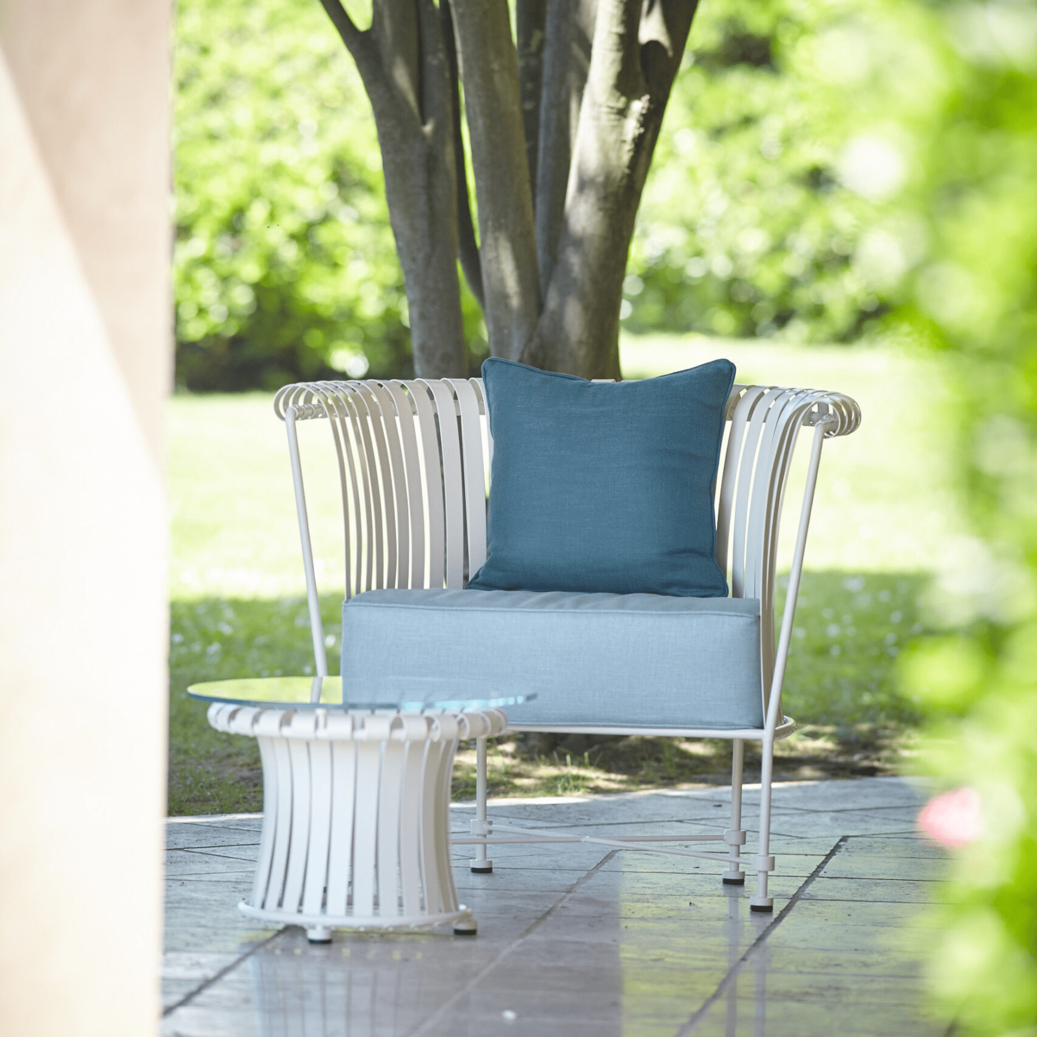 Elegant Iron Patio Armchair placed outdoors with a blue cushion, paired with a matching coffee table. | High End Outdoor Armchair | Luxury Metal Patio Furniture | Designed and Made in Italy