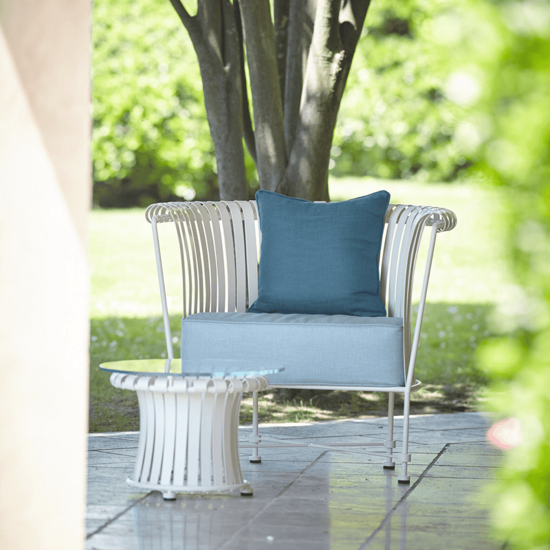 Elegant Iron Patio Armchair placed outdoors with a blue cushion, paired with a matching coffee table. | High End Outdoor Armchair | Luxury Metal Patio Furniture | Designed and Made in Italy